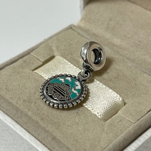 May include: Silver charm featuring a blue and white enamel design of a building with the text "Folly Beach" on it. The charm has a silver loop for attaching to a bracelet.