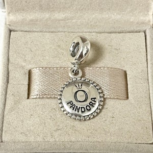 May include: A silver charm with a round, silver charm with a black 'O' and the word 'PANDORA' around it. The charm has a small crown above the 'O'.