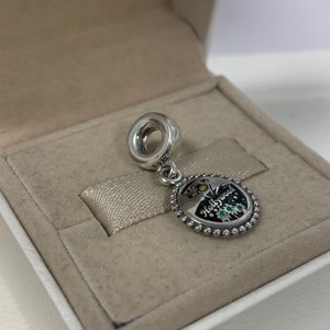 May include: Silver charm featuring a black and white enamel design of the Hollywood sign and palm trees. The charm has a silver ring at the top for attaching to a bracelet.