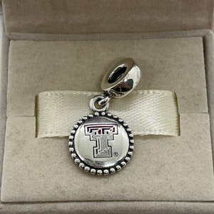 May include: Silver charm with a red and white Texas Tech University logo on a round charm with a beaded border.