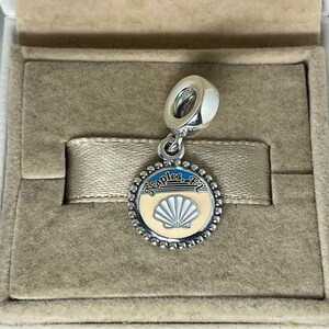 May include: Silver charm with a white seashell and blue water design. The charm says "Naples, FL" on the top.