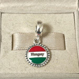 May include: A silver charm with a red, white, and green enamel circle featuring the word "Hungary".