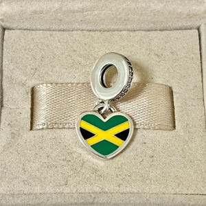 May include: A silver charm in the shape of a heart with the Jamaican flag colors: green, yellow, and black.
