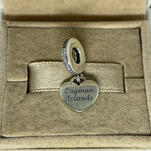 May include: Silver charm with a heart-shaped pendant that reads "Cayman Islands". The charm is in a velvet-lined box.