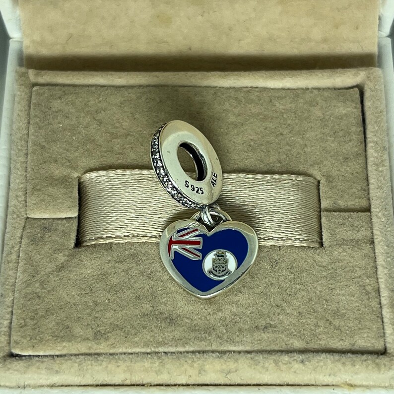 May include: A silver charm in the shape of a heart with the flag of Bermuda on one side and the Bermuda coat of arms on the other. The charm is attached to a silver chain with a small silver bead.