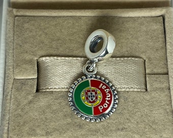 May include: A silver charm with a round, enamel-painted design featuring the Portuguese flag and the word "Portugal" in white lettering.