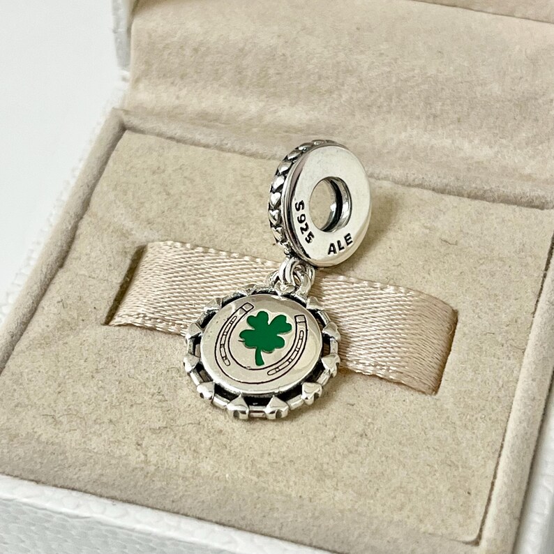 May include: Silver charm with a green four-leaf clover and horseshoe design. The charm is marked with "S925 ALE".