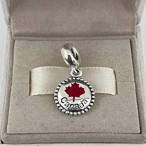 May include: Silver charm with a red maple leaf and the word "Canada" on a circular pendant.
