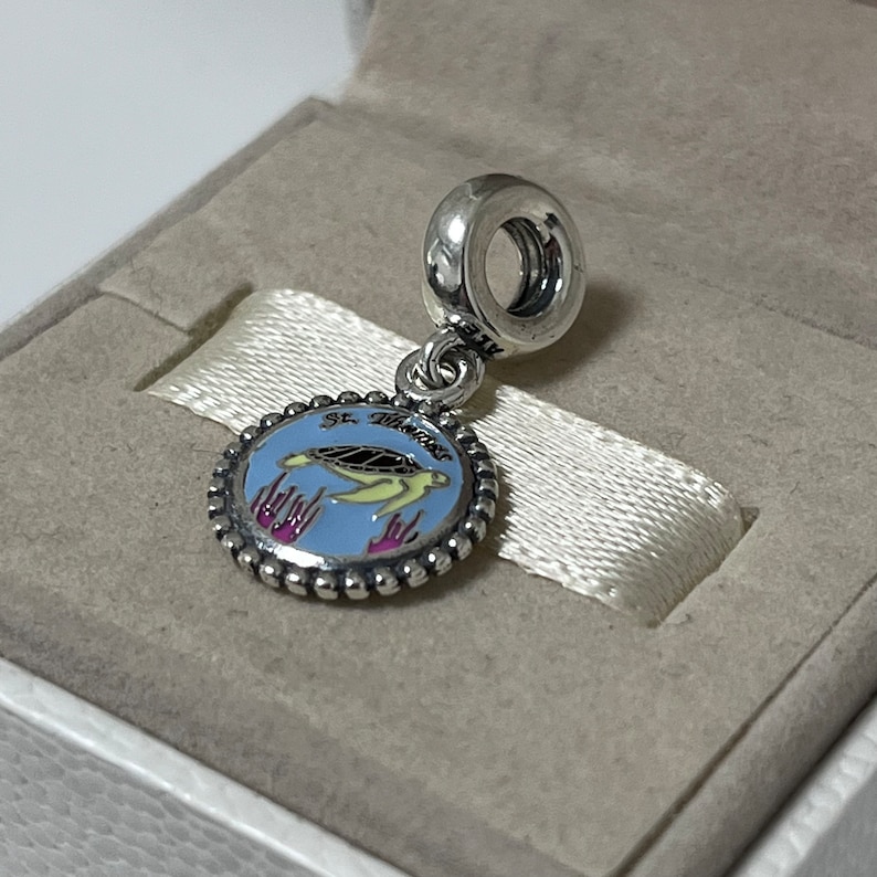 Puede incluir: Un charm de plata con un c&iacute;rculo de esmalte azul que presenta una tortuga marina amarilla y el texto "St. Maarten". El charm tiene un borde de cuentas de plata y un lazo de plata para sujetarlo a una pulsera.