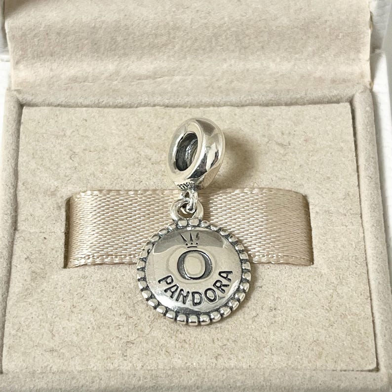 May include: A silver charm with a round pendant featuring the word "Pandora" and a crown above the letter "O".
