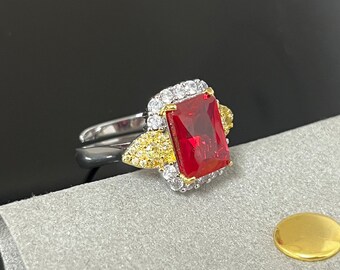 Könnte beinhalten: Ein silberner Ring mit einem großen quadratischen roten Edelstein, der von kleineren klaren und gelben Edelsteinen umgeben ist.
