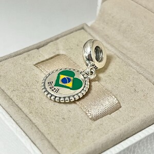 May include: Silver charm with a green heart featuring the Brazilian flag and the word "Brazil" in a circle around the heart.