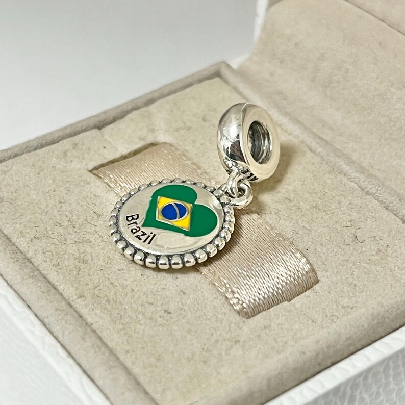 May include: Silver charm with a green heart featuring the Brazilian flag and the word "Brazil" in a circle around the heart.