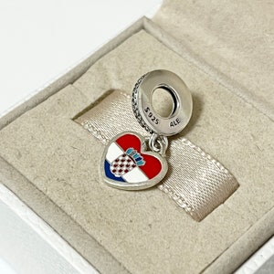 Puede incluir: Un charm de plata en forma de coraz&oacute;n con la bandera croata en &eacute;l. El charm est&aacute; unido a una cadena de plata con una cuenta redonda que dice "S925 ALE".