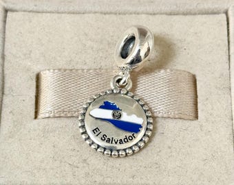 May include: Silver charm featuring a blue and white outline of El Salvador with the country's flag inside. The charm is attached to a silver loop.