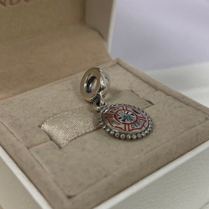 May include: Silver charm with a red and white enamel fire department logo. The logo features a fire hydrant, an axe, and a ladder. The charm is in a white box.