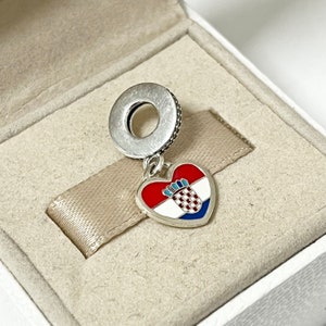 Puede incluir: Un charm de plata en forma de coraz&oacute;n con la bandera croata en &eacute;l. El charm cuelga de un anillo de plata.