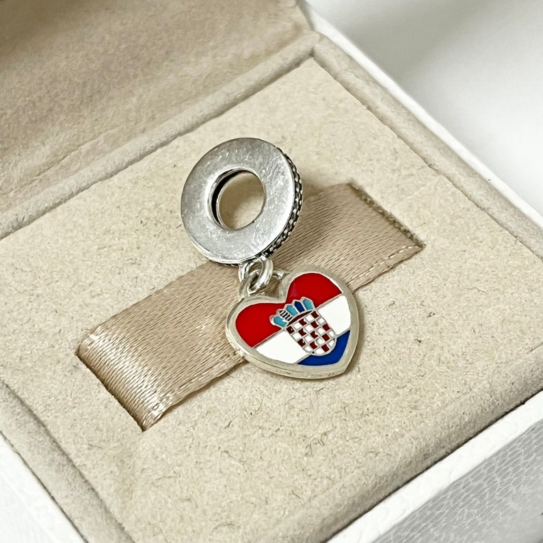 Puede incluir: Un charm de plata en forma de coraz&oacute;n con la bandera croata en &eacute;l. El charm cuelga de un anillo de plata.