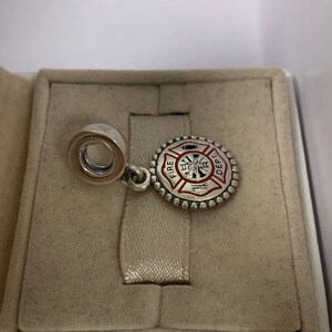 May include: Silver charm with a red and white enamel fire department logo. The logo features a firefighter with an axe and a hose, and the words "FIRE DEPT."