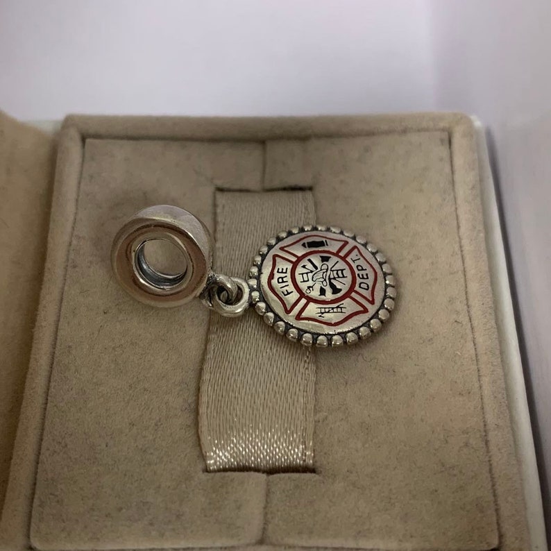 May include: Silver charm with a red and white enamel fire department logo. The logo features a firefighter with an axe and a hose, and the words "FIRE DEPT."