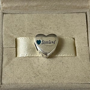 May include: Silver charm in the shape of a heart with a smaller blue heart and the word "Scotland" inscribed on it.