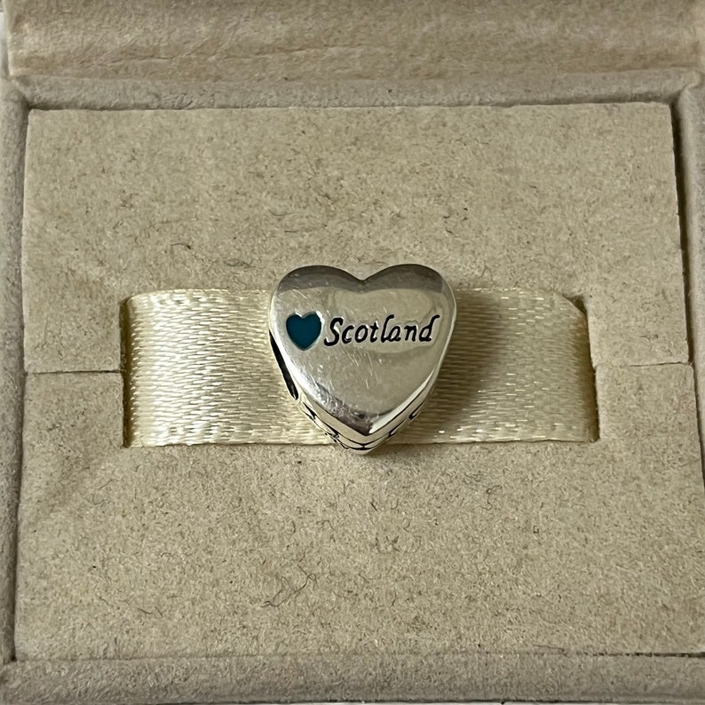 May include: Silver charm in the shape of a heart with a smaller blue heart and the word "Scotland" inscribed on it.