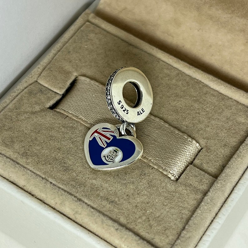 May include: Silver charm in the shape of a heart with a blue and red flag design. The charm has a silver ring with the text "S925 ALE" on it.