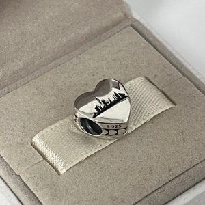 Może przedstawiać: Srebrny charm w kształcie serca z sylwetką miasta w środku. Charm ma mały otw&oacute;r do przymocowania do bransoletki. Tył charmu jest wytłoczony "S 925".