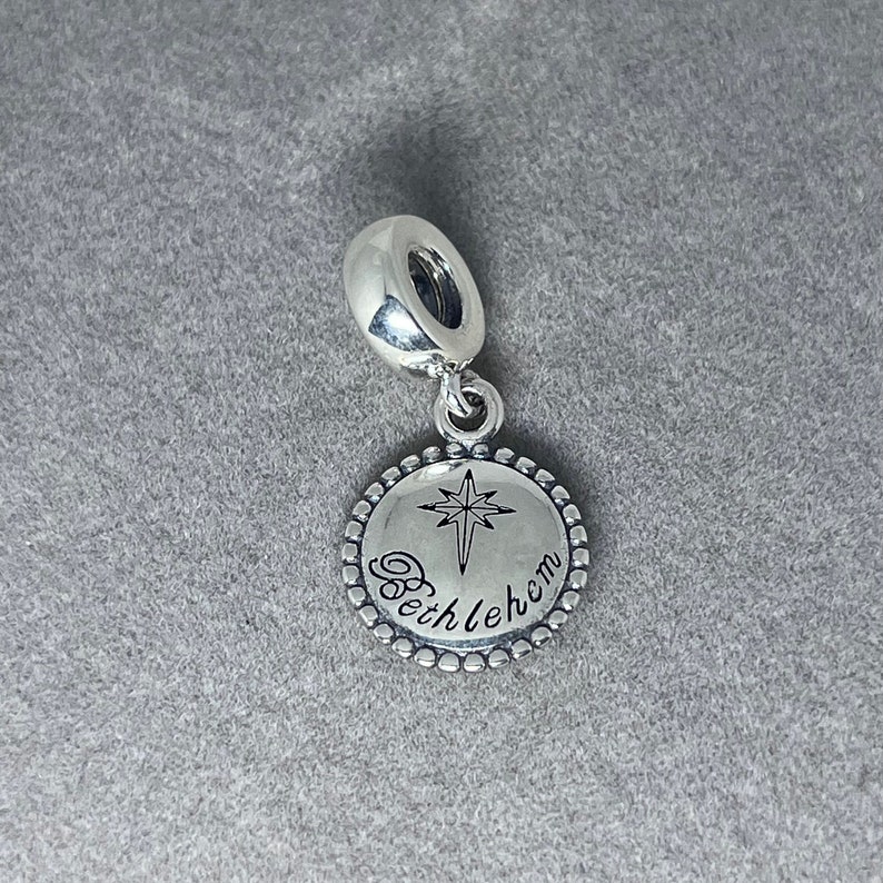 May include: Silver charm with a round pendant featuring a star of Bethlehem and the word "Bethlehem" engraved on it.