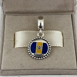 Op de afbeelding: Zilveren bedel met een blauw en geel emaille ontwerp van de vlag van Barbados. De bedel heeft een parelrand en het woord "Barbados" staat onder de vlag.