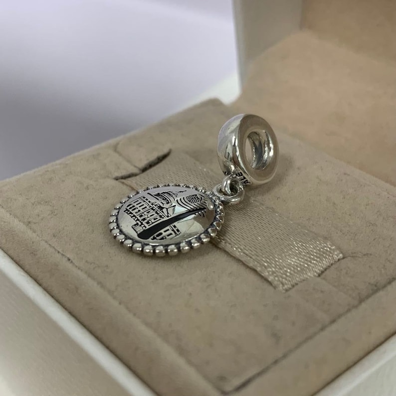 Puede incluir: Un charm de plata con una imagen detallada de un edificio, posiblemente un monumento europeo, con una cuenta redonda de plata en la parte superior.