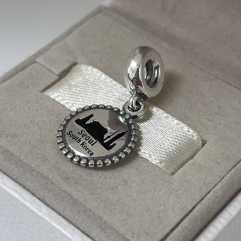 May include: Silver charm featuring a black and white image of the Seoul skyline with the text "Seoul South Korea".