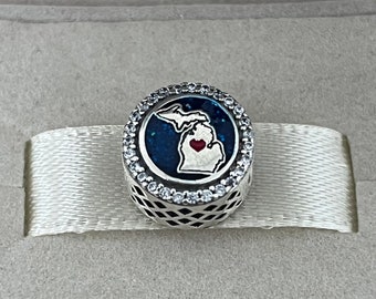 Op de afbeelding: Een zilveren bedel met een blauwe en witte emaille omtrek van de staat Michigan met een rood hart in het midden. De bedel is omgeven door een cirkel van heldere zirkonia stenen.