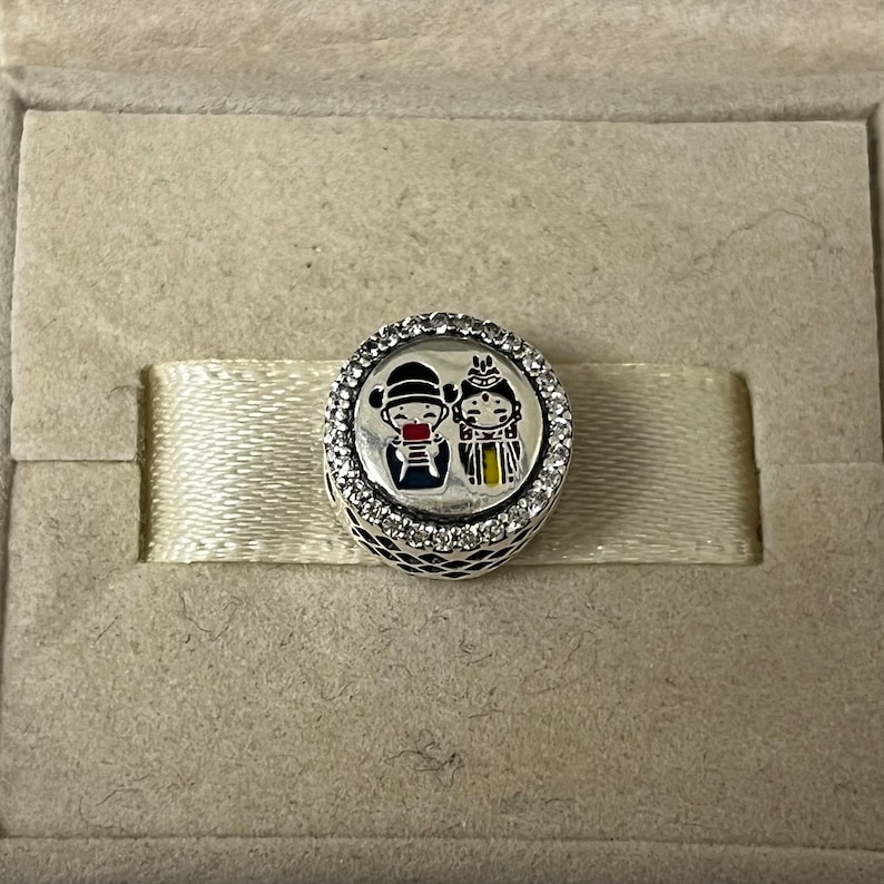 May include: Silver charm with a white background and a colorful image of a couple in traditional Chinese clothing. The charm is surrounded by a circle of clear cubic zirconia stones.
