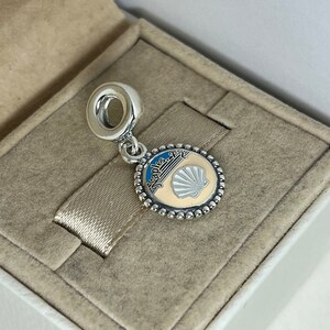 May include: Silver charm with a blue and white enamel design featuring a seashell and the text "Naples, FL".