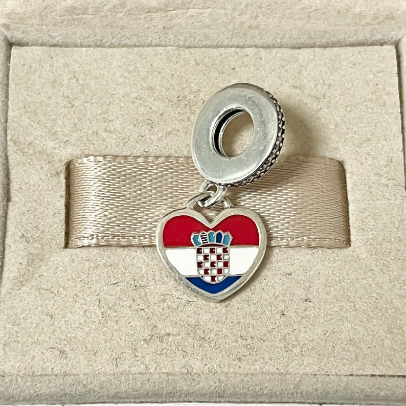 Puede incluir: Un charm de plata en forma de coraz&oacute;n con la bandera croata en &eacute;l. El charm est&aacute; unido a un anillo de plata.