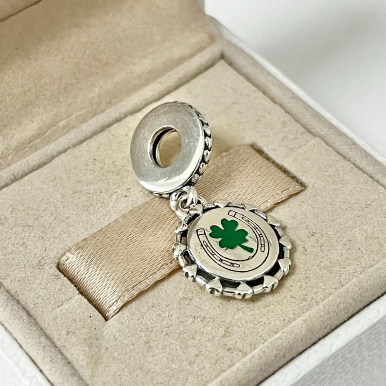May include: Silver charm with a green four-leaf clover and horseshoe design. The charm is attached to a silver bead.
