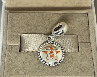 May include: A silver charm with a white star and orange "H" in the center, representing the Houston Astros baseball team. The charm is in a small, velvet-lined box.