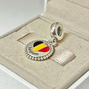 Pode incluir: Berloque de prata com um design de esmalte em forma de cora&ccedil;&atilde;o que apresenta as cores da bandeira belga, preto, amarelo e vermelho. O berloque tamb&eacute;m tem a palavra "B&eacute;lgica" inscrita ao redor do cora&ccedil;&atilde;o.