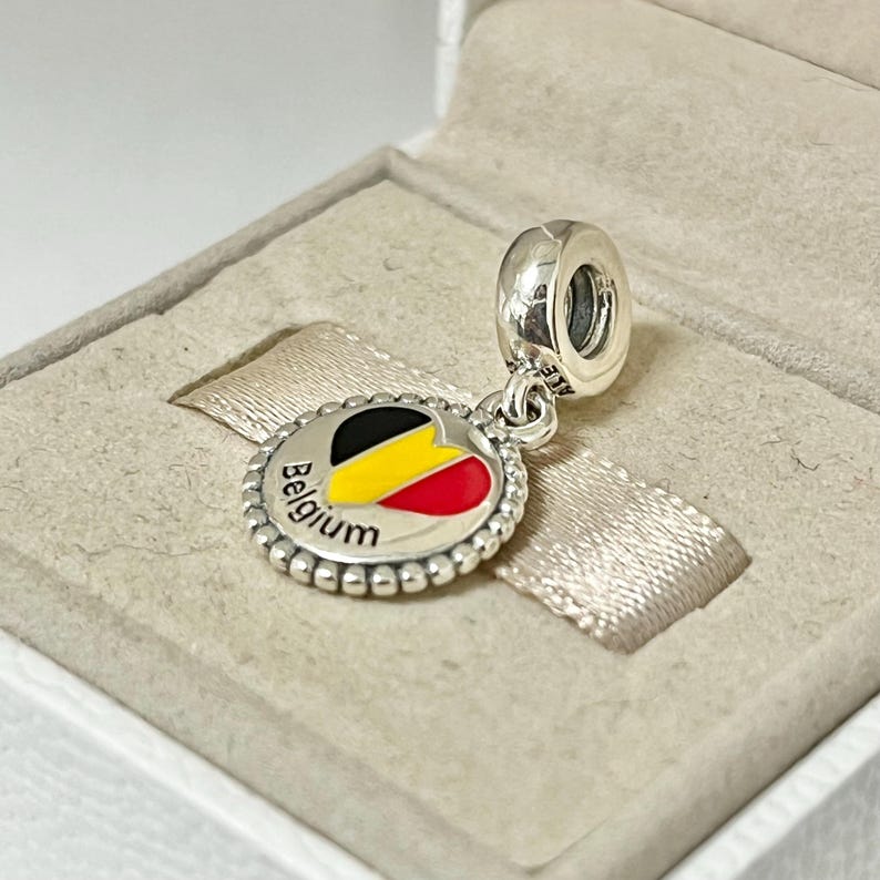 Pode incluir: Berloque de prata com um design de esmalte em forma de cora&ccedil;&atilde;o que apresenta as cores da bandeira belga, preto, amarelo e vermelho. O berloque tamb&eacute;m tem a palavra "B&eacute;lgica" inscrita ao redor do cora&ccedil;&atilde;o.
