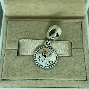 May include: Silver charm with a colorful rooster and the words "Key West" on a round, beaded border.