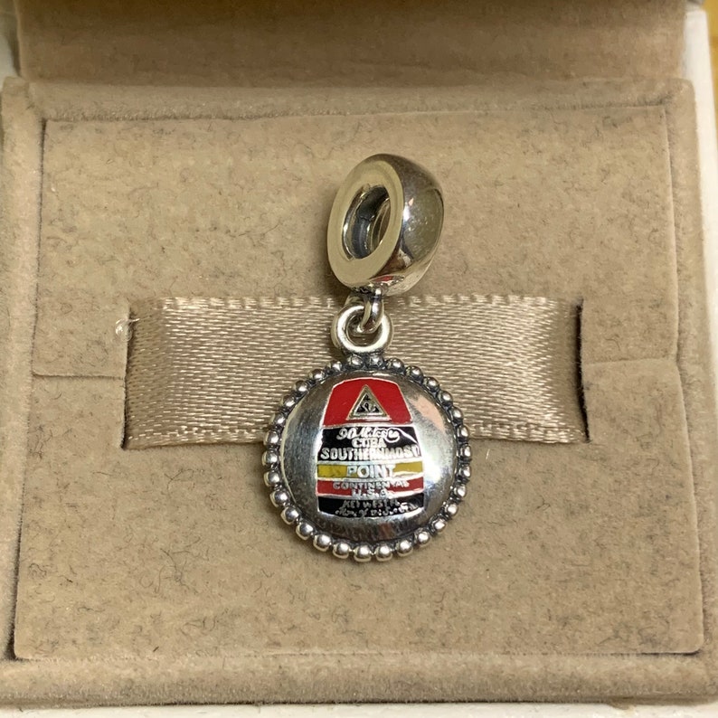 May include: Silver charm with a red, yellow, and black enamel design. The charm features the text "SOUTHERNMOST POINT" and "CONTINENTAL USA".