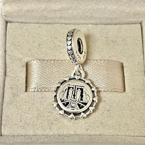 Puede incluir: Un charm de plata con una detallada representación en blanco y negro del puente de Brooklyn. El charm tiene un colgante redondo con un borde en forma de corazón y una fianza de conexión con detalles de corazón. El charm está suspendido de una fianza de plata con la inscripción "S925 ALE".