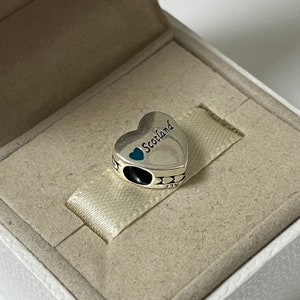 May include: Silver charm in the shape of a heart with the word "Scotland" and a blue heart on it.
