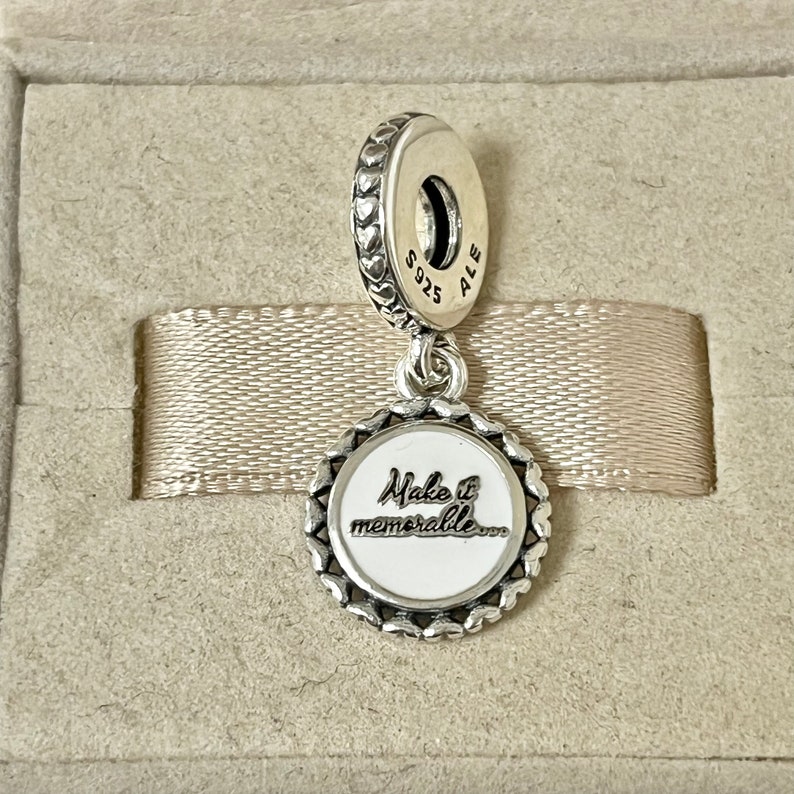 Puede incluir: Encanto de plata con un c&iacute;rculo de esmalte blanco que dice "Make it memorable..." y un borde en forma de coraz&oacute;n. La parte posterior del encanto tiene la inscripci&oacute;n "S925 ALE".