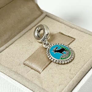 May include: Silver charm with a blue and green enamel design featuring a silhouette of a moose and the word "Alaska".