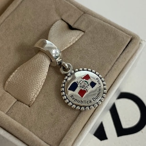 May include: Silver charm with a round, silver-rimmed pendant featuring the Dominican Republic flag and the text "Republica Dominicana".