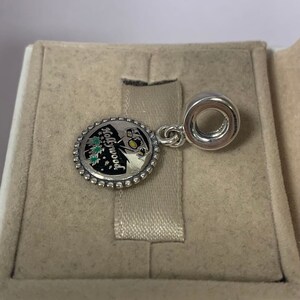 May include: Silver charm featuring a black and white image of the Hollywood sign and palm trees. The charm has a gold inscription reading "Hollywood" and is accented with green enamel. The charm is attached to a silver ring.