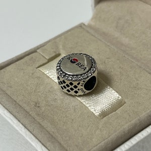 May include: Silver charm with a round, black and white patterned design. The charm features a silver circle with a red, white, and blue Korean flag and the word "KOREA" in white lettering.