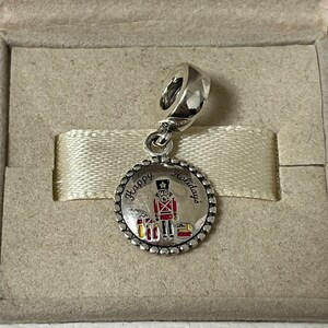 May include: Silver charm with a red and white toy soldier and the words "Happy Holidays" on a silver circle.